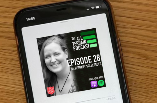A photo of Dr. Bethany Sollereder and The All Terrain Podcast artwork on a mobile phone