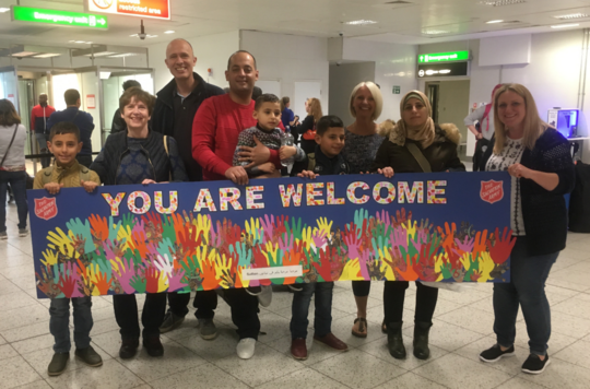 A Salvation Army group at the airport ready to welcome refugees with a sign that reads 'You are welcome'