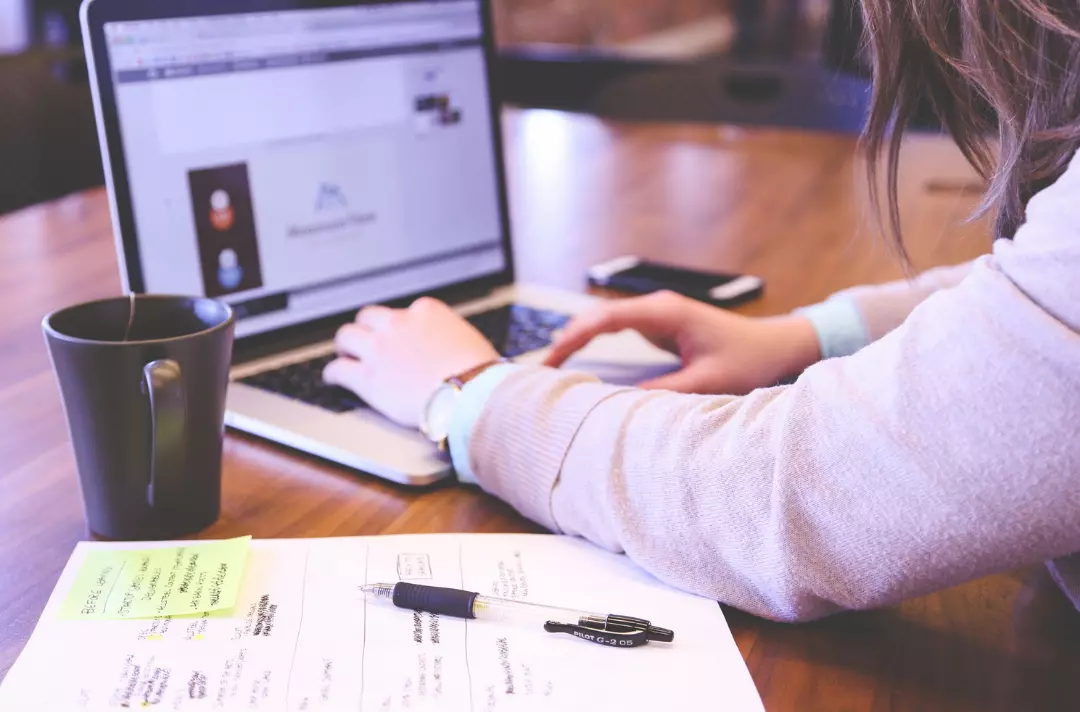 A women working at a laptop with pen and paper ready