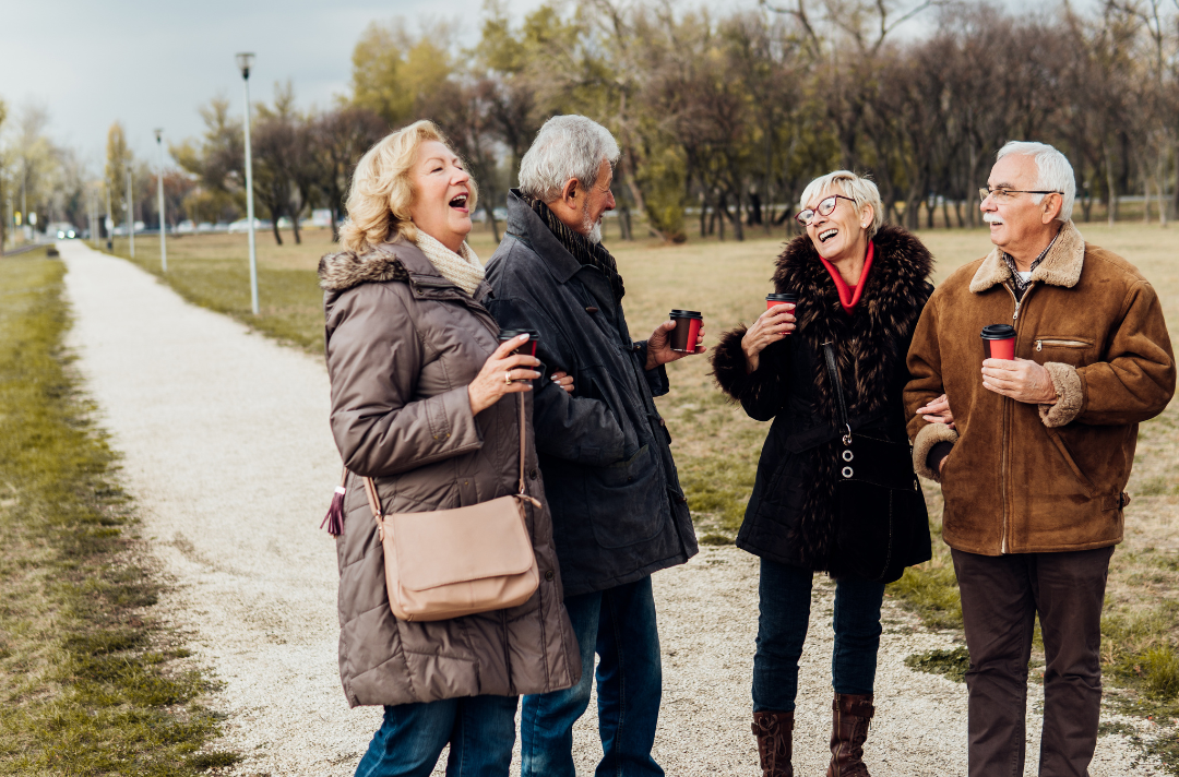 Two older couples walking and laughing holding coffee
