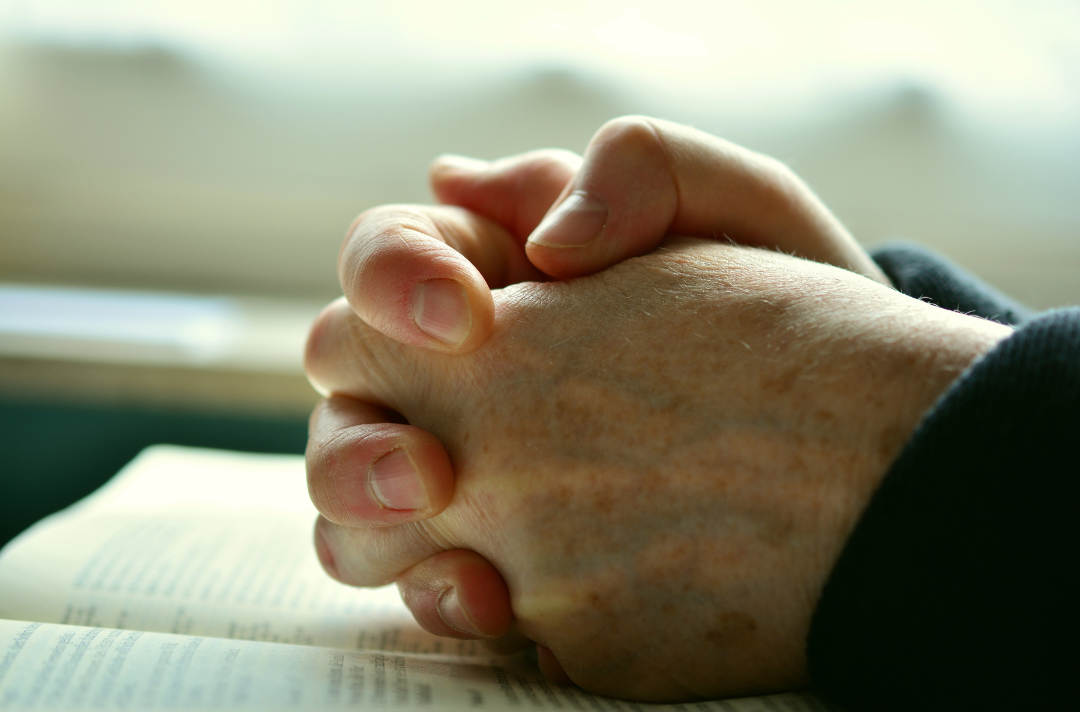 Clasped hands in prayer resting on the Bible