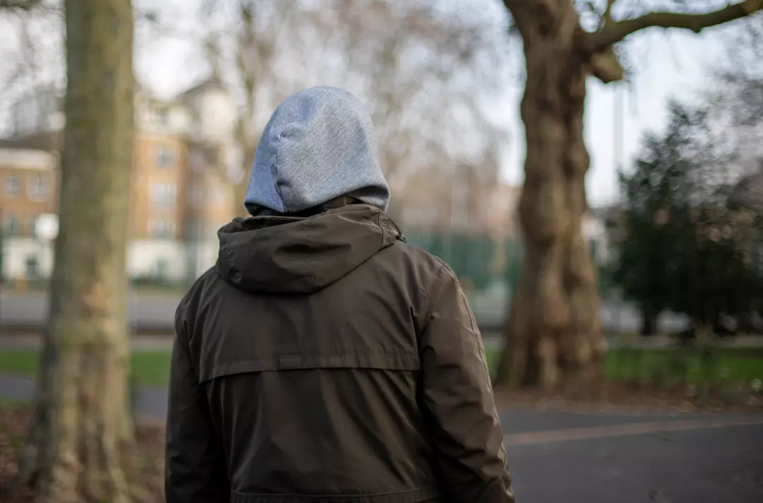 Someone walking through a park with their hood up