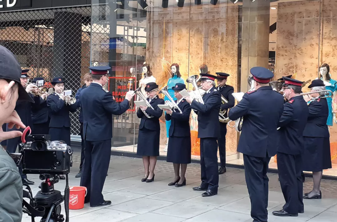 A camera operator filming Regent Hall Band playing on Oxford Street