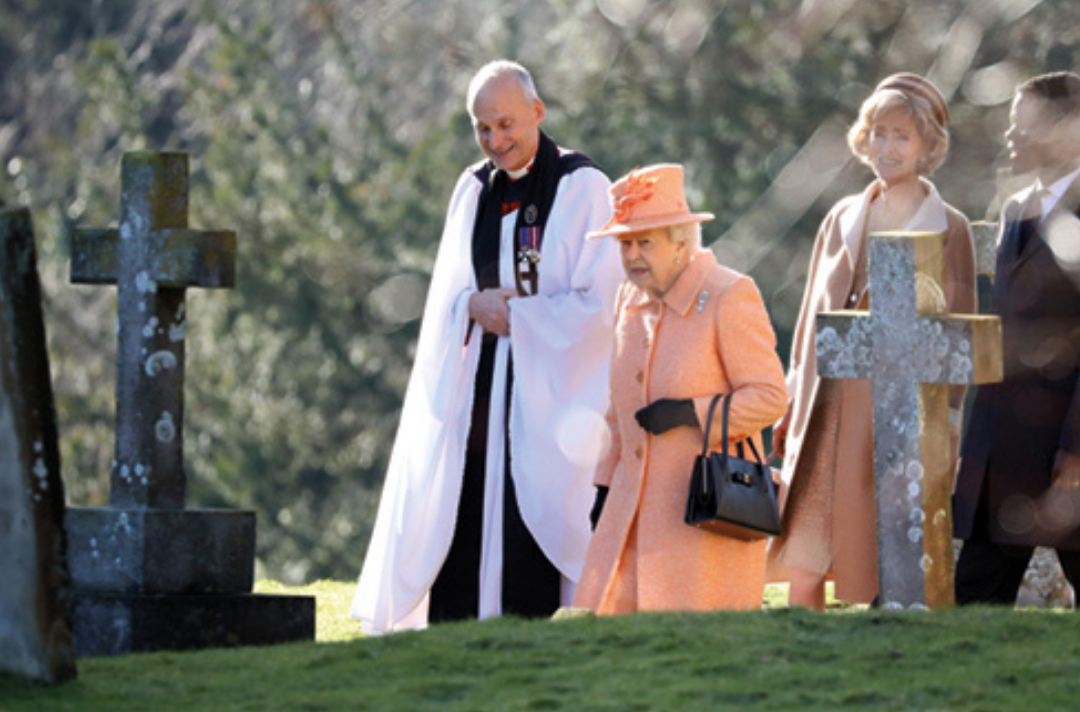 The Queen walking through a church yard with a vicar and members of the congregation