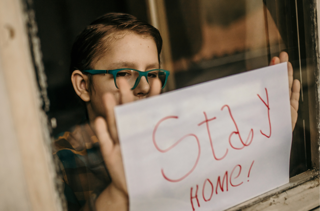 A child putting up a home made sign that reads 'stay at home' in the window