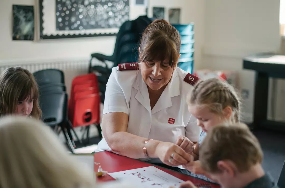 A lady in Salvation Army woman helping a child with crafts