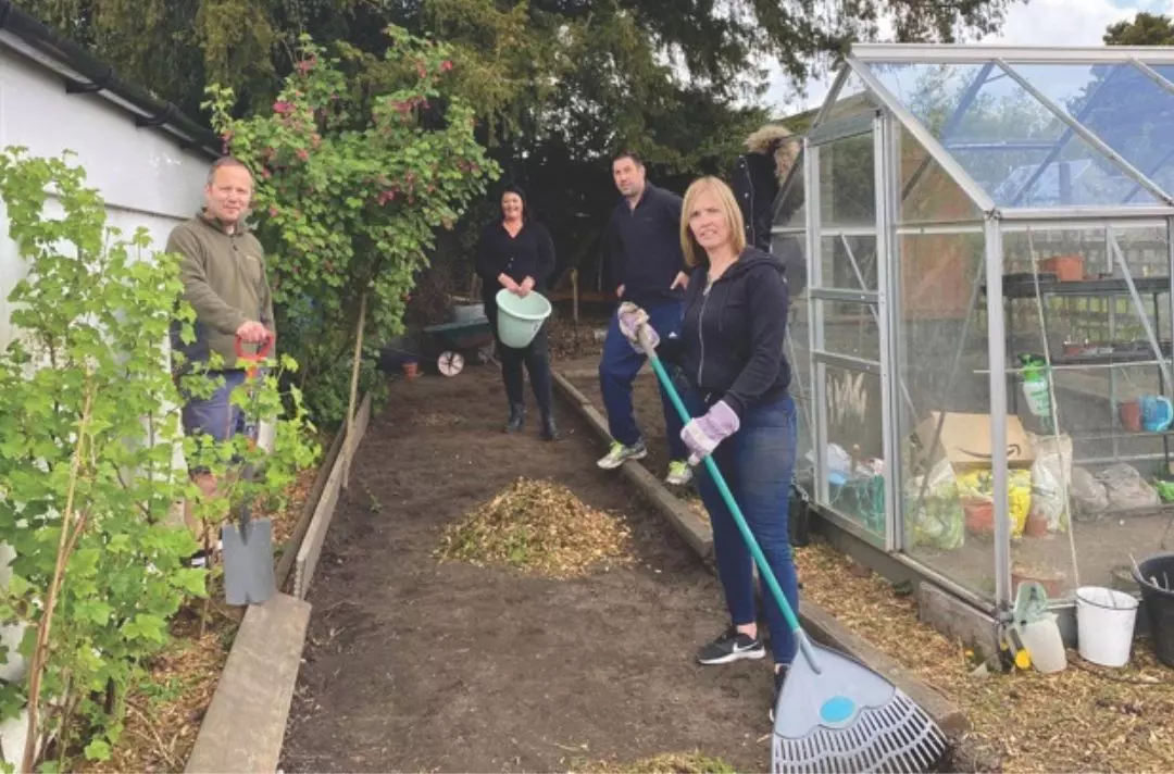 People with spades, buckets and rakes in a garden by a greenhouse