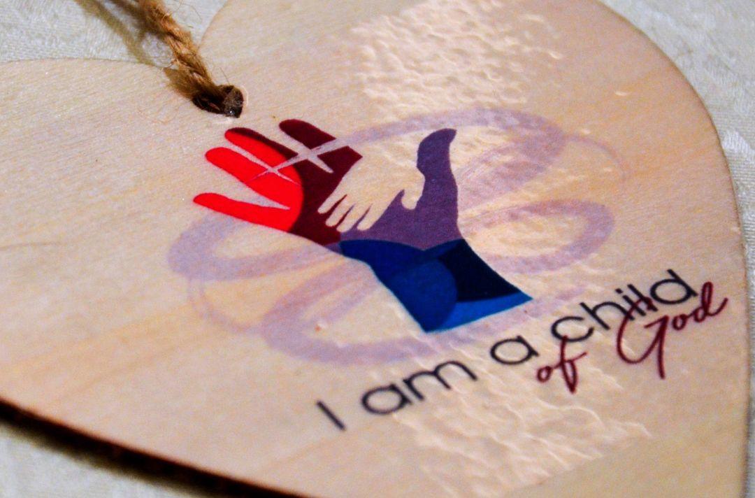 A wooden heart with the words 'I am a child of God' and a graphic of a small hand in a bigger hand