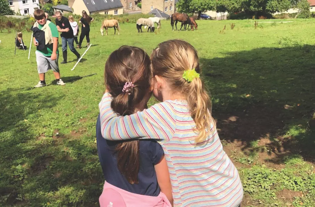 Two children hugging in a field with horses
