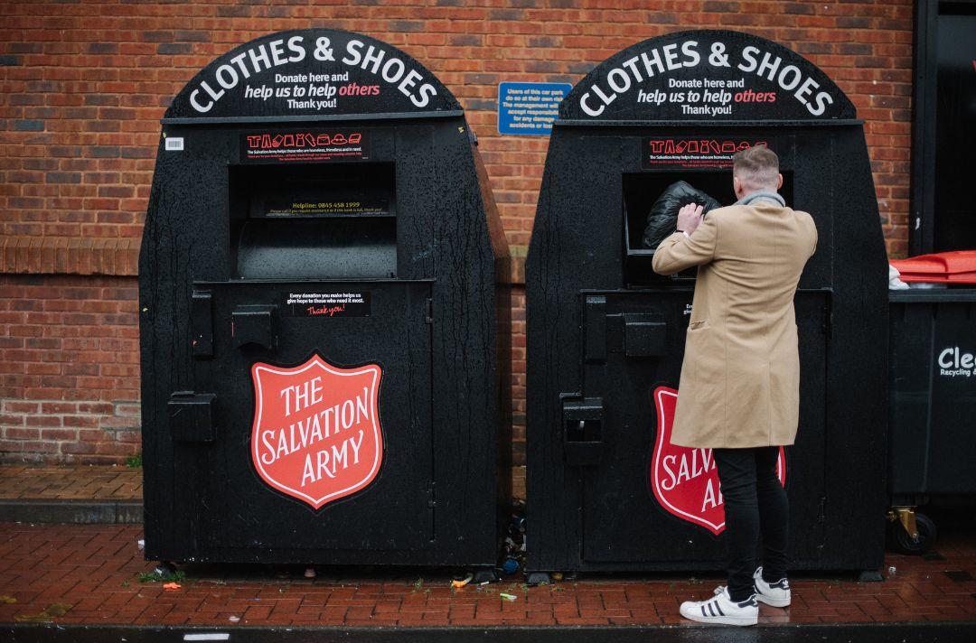 Someone putting a bag of clothes into a Salvation Army clothing bank