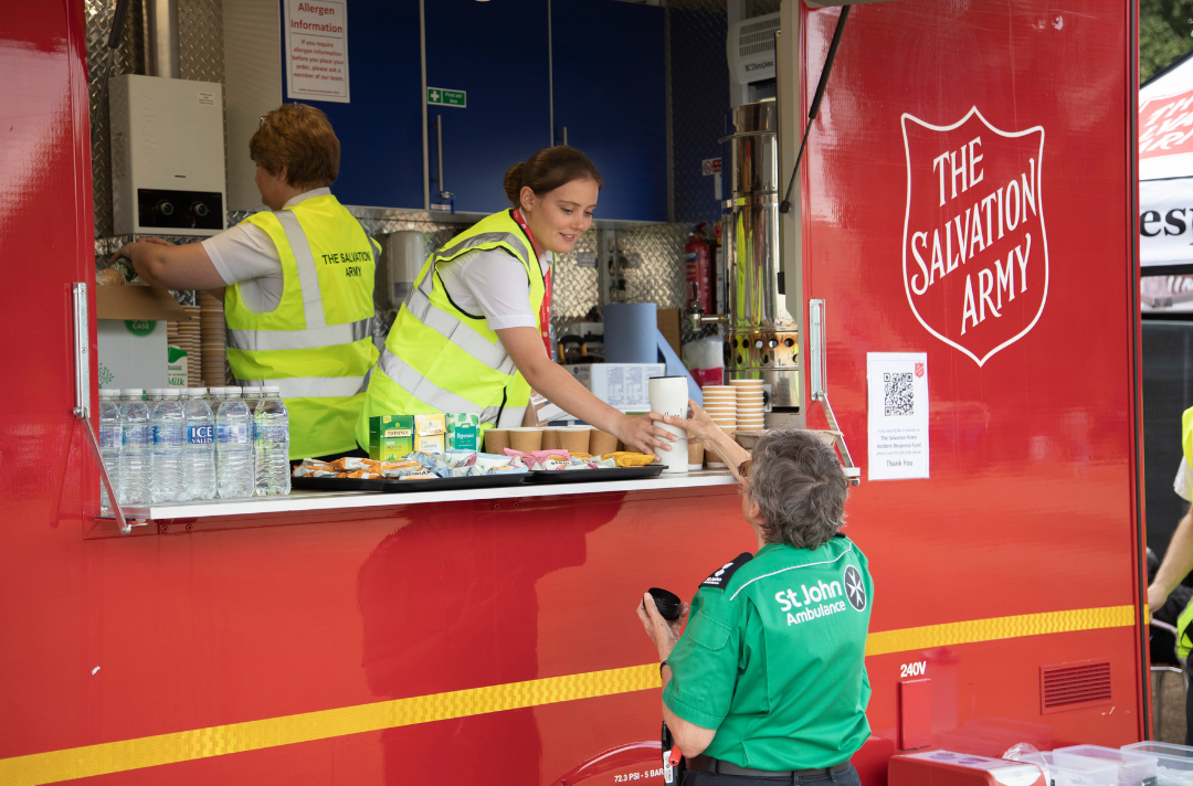 A Salvation Army volunteer serves a St John Ambulance volunteer a hot drink