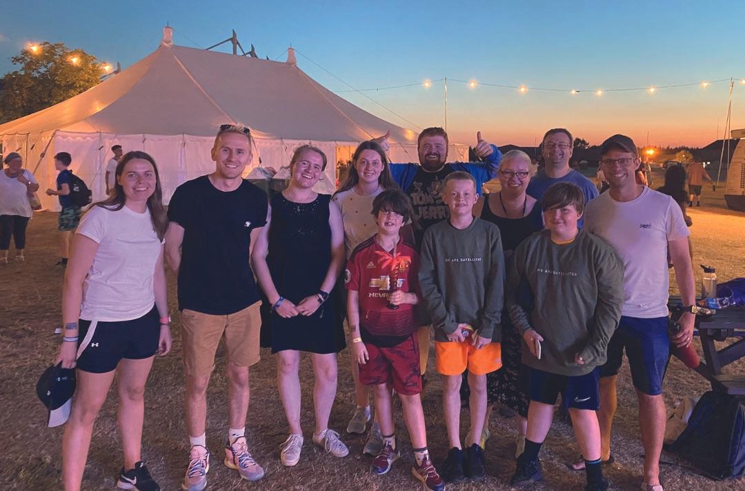 A group of teenagers and young adults in a field at dusk with a marquee behind them
