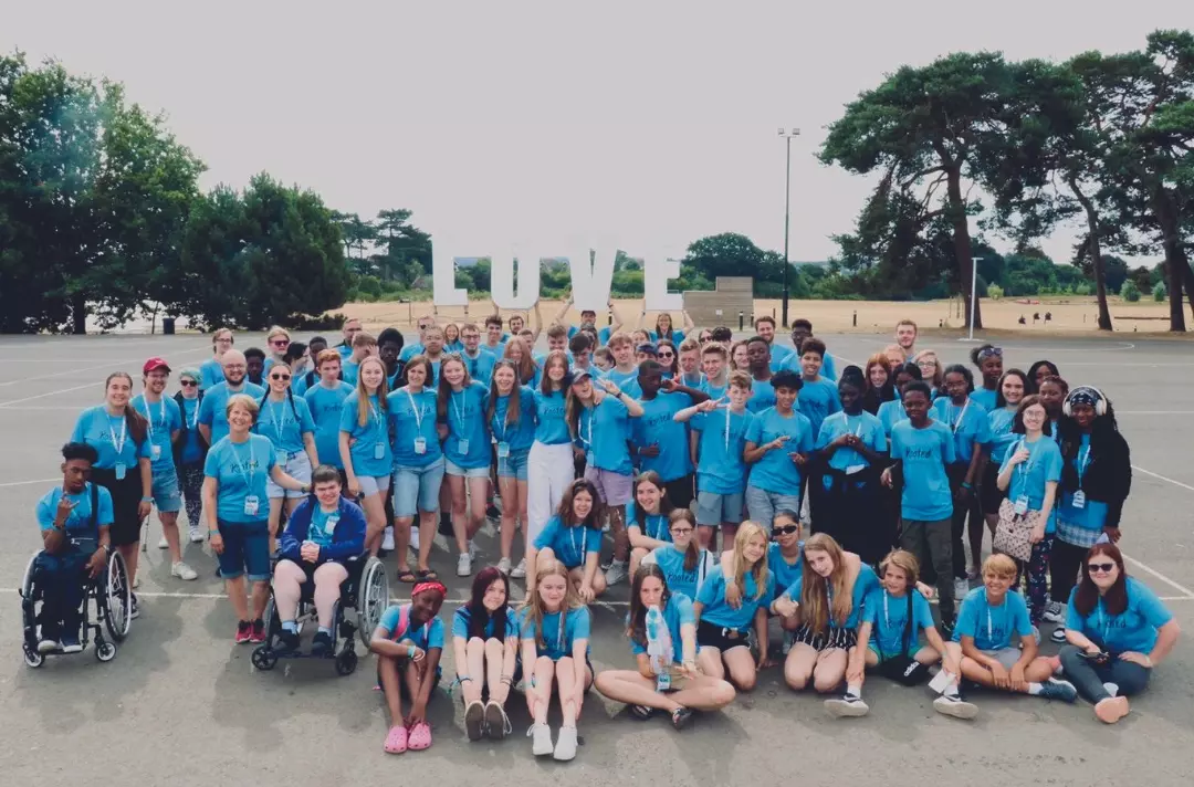 A large group of teenagers and adults in a playground with the word 'love' spelled out in large letters behind them