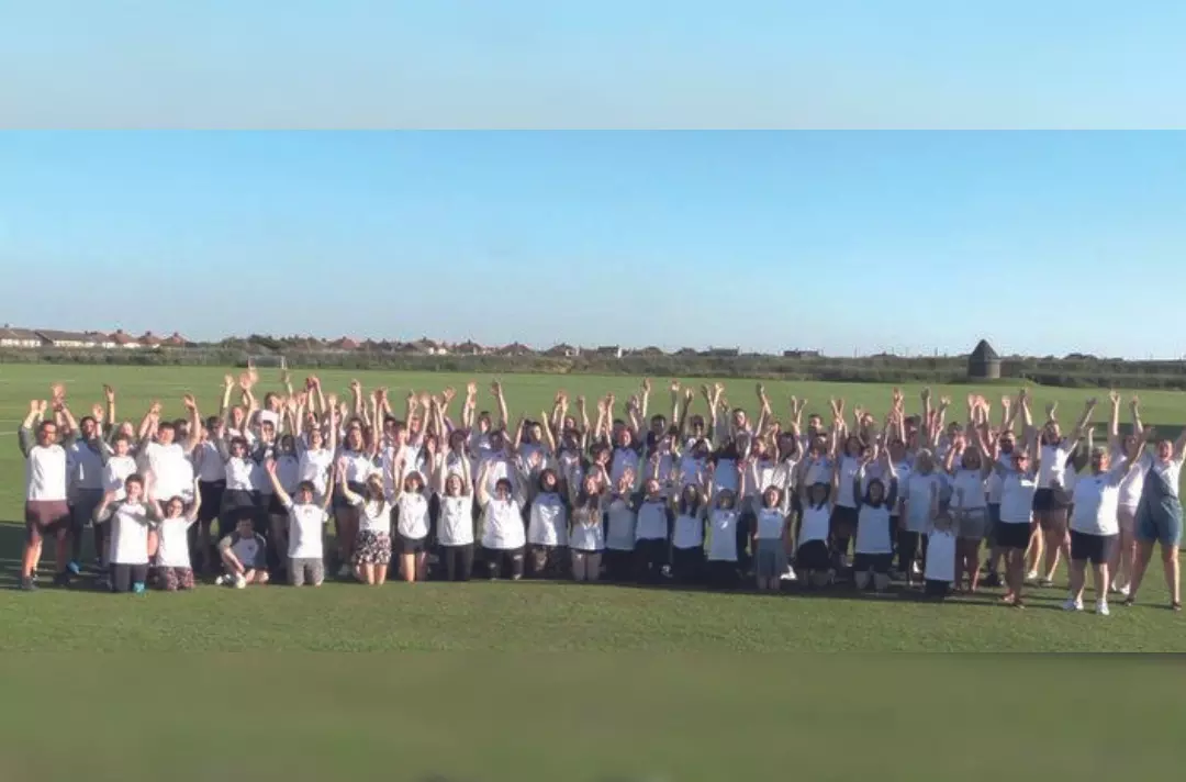 A large group of teenagers and adults with their hands in the air in a field
