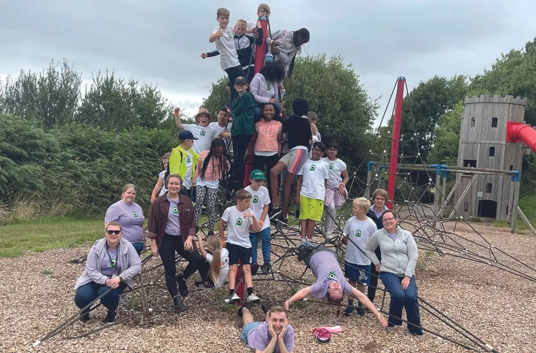 A group of children climbing in a playground with adults standing nearby