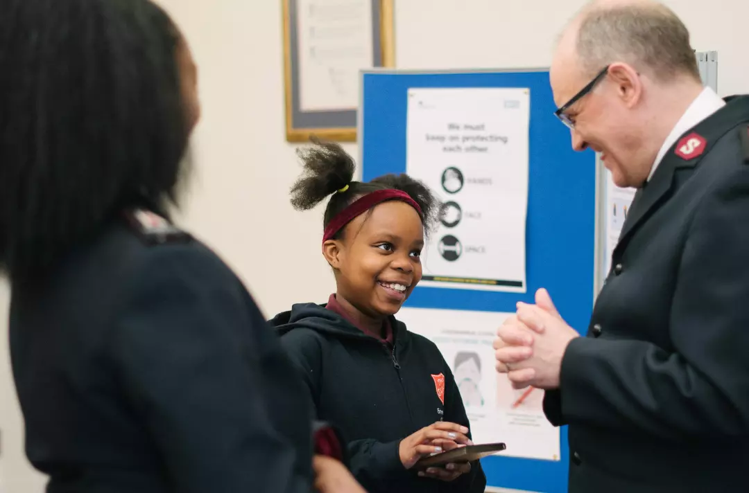 A girl holding a mobile phone and wearing a Salvation Army red shield jumper talking to a Salvation Army office