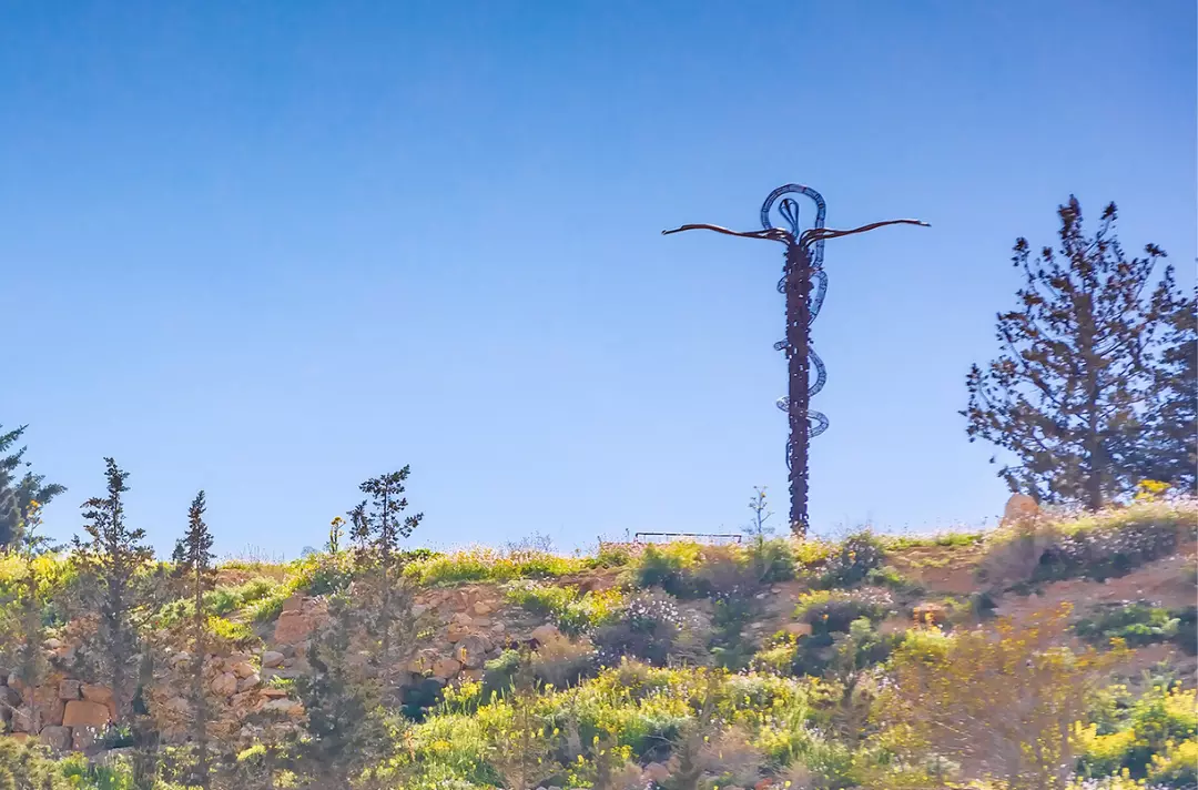 A cross status with a serpent wrapped around it on a mountain side