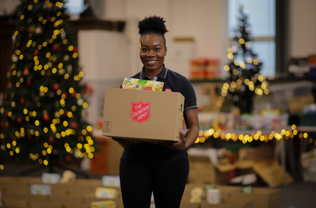 Someone holding a box of food with The Salvation Army red shield on it