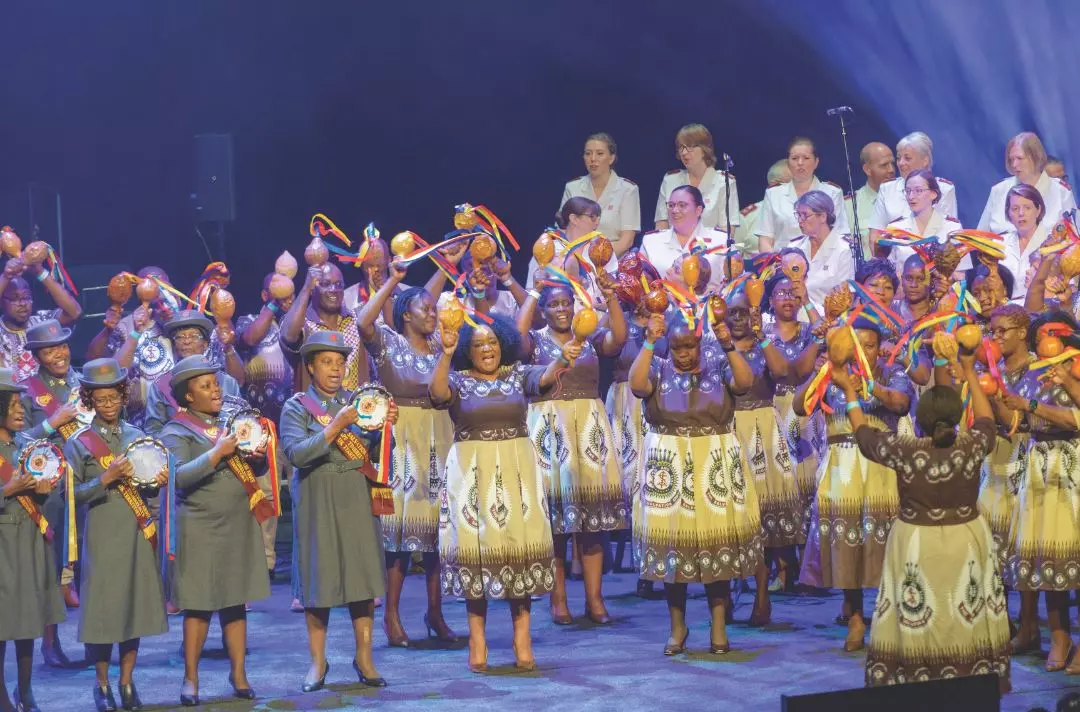 A large group of people dancing with timbrels and percussion in different styles of African Salvation Army uniform