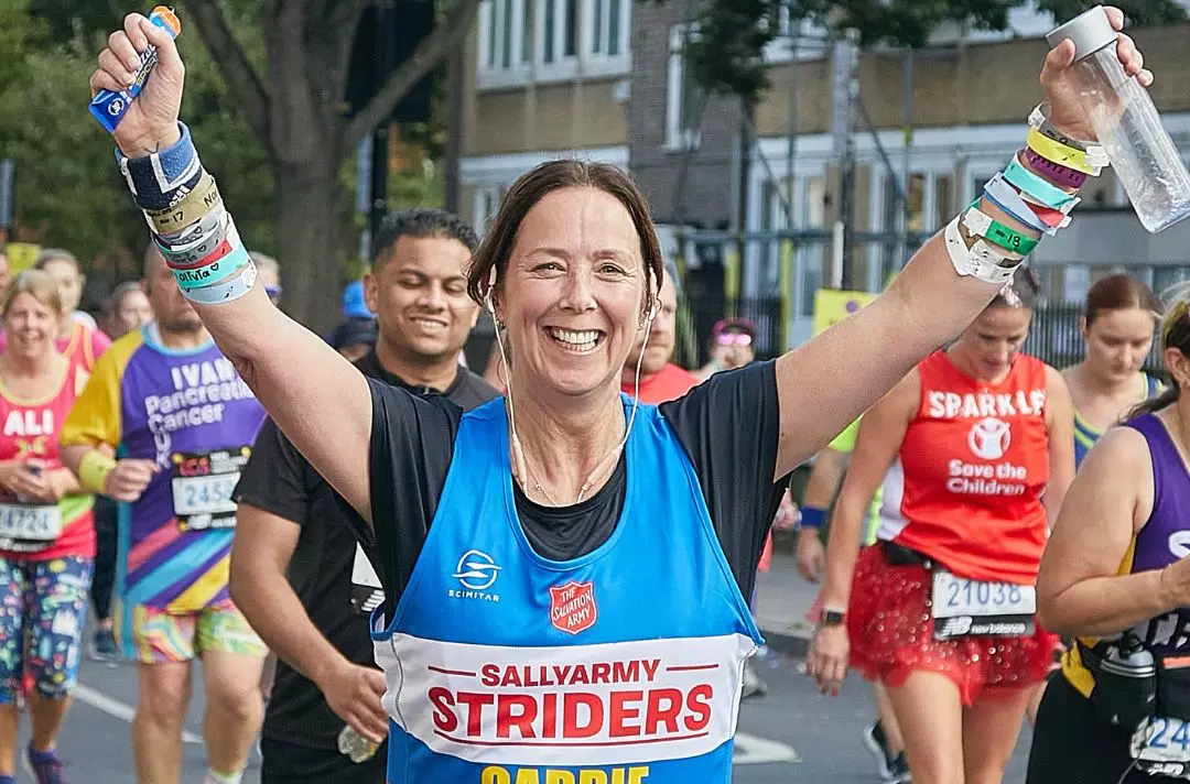Someone running in a race wearing a Salvation Army running vest with their hands in the air