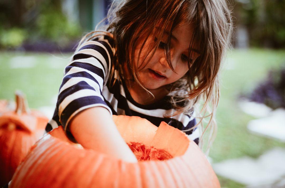 A photo of a child putting their hand inside a pumpkin