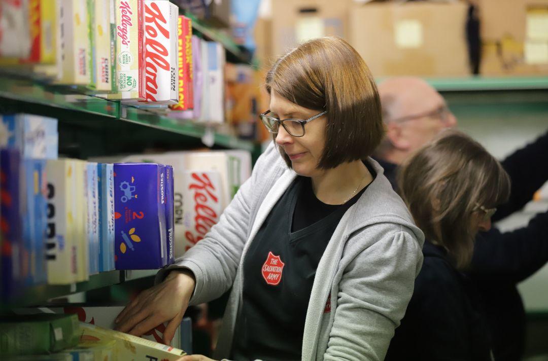 Someone taking a box of cereal from a food bank pantry