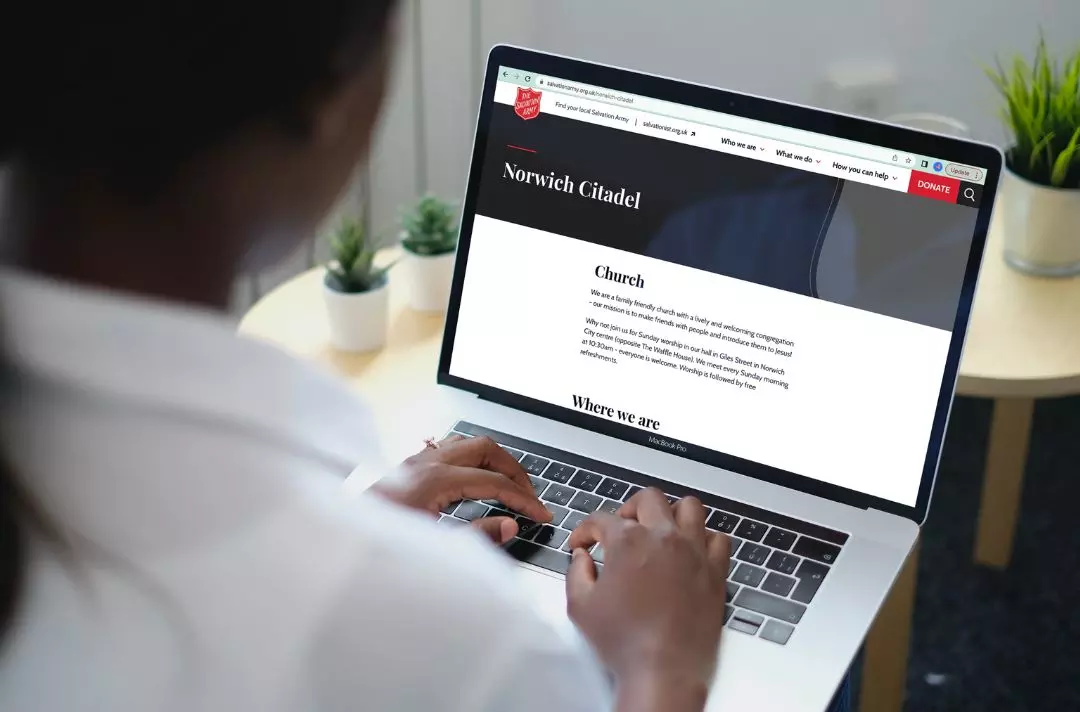 Someone working on a laptop. A Salvation Army webpage is on the screen.