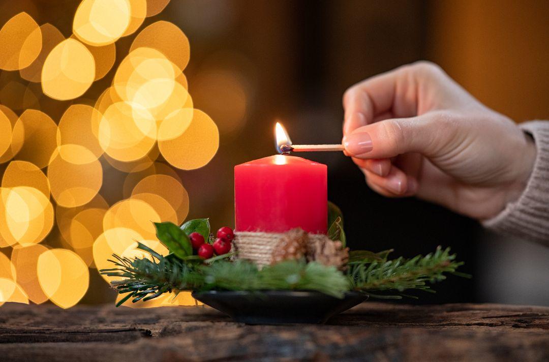 A photo of someone lighting a red candle with Christmas foliage around it