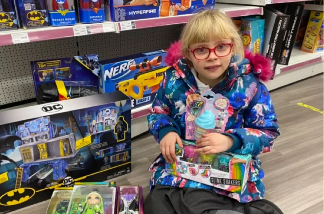 A photo of Lottie sitting on the floor of The Entertainer toy shop surrounded by toys