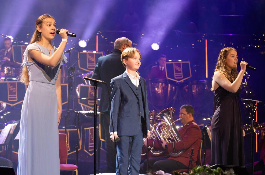 A photo of Erin Moir, Cormac Thompson and Anna Sharman singing on the stage of the Royal Albert Hall wearing smart clothes