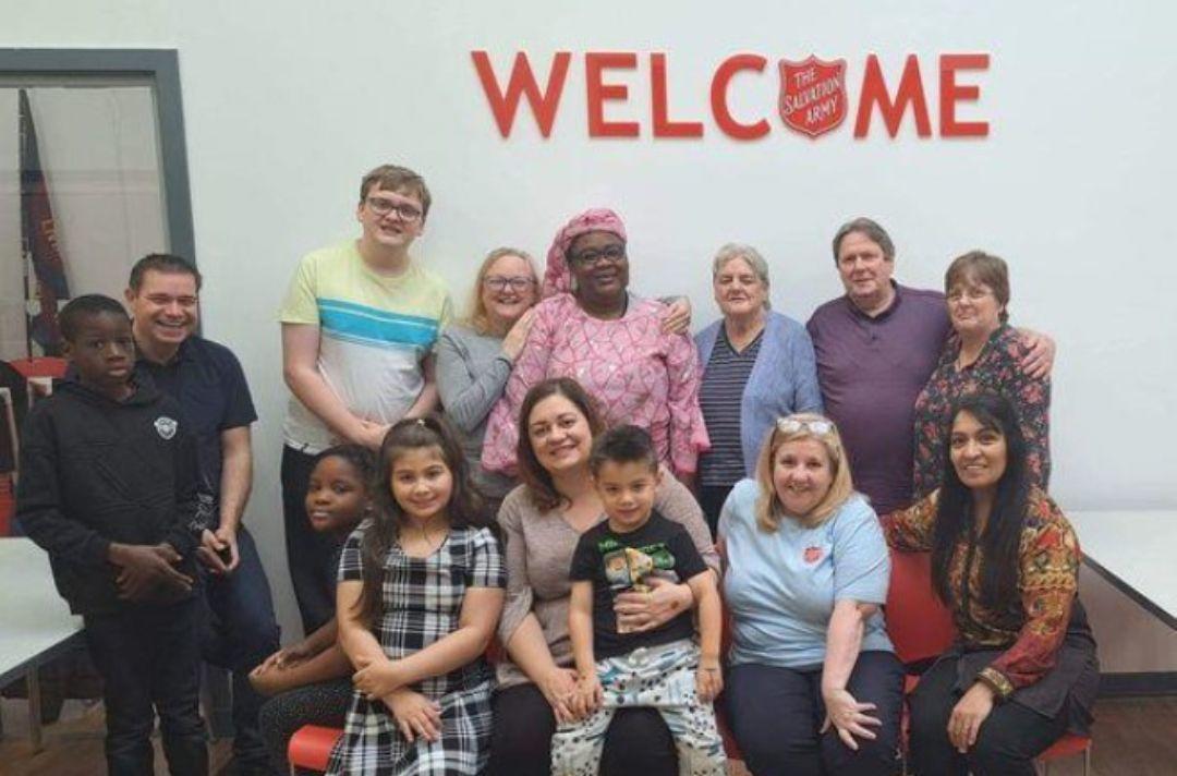 A diverse group of people posing for a photo beneath a Salvation Army branded welcome sign