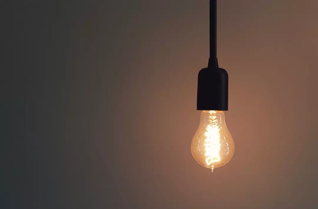 The photo shows a bare lightbulb with an orange glow hanging in front of a plain grey background.