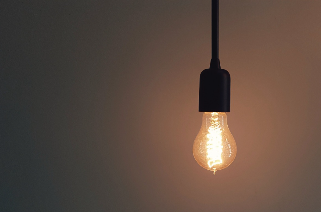 The photo shows a bare lightbulb with an orange glow hanging in front of a plain grey background.