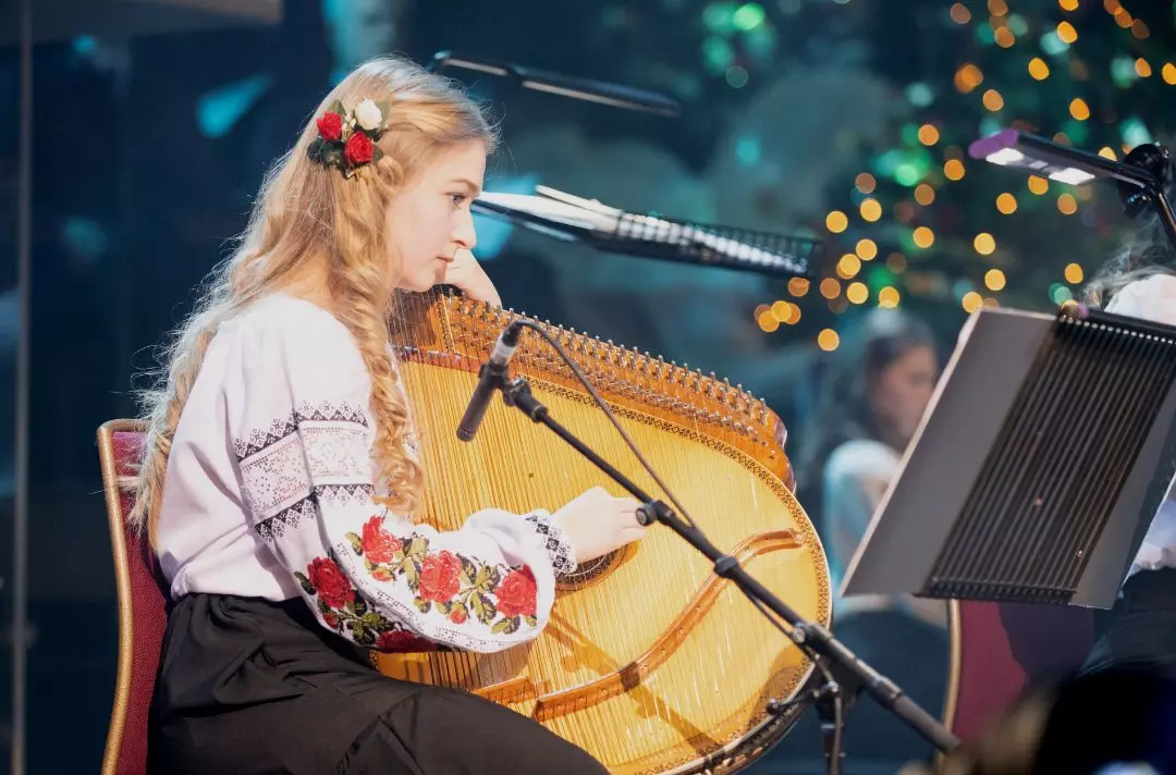 A photo of a women playing a bandura, a traditional Ukrainian stringed instrument, on the stage of the Royal Albert Hall andand wearing traditional Ukrainian dress