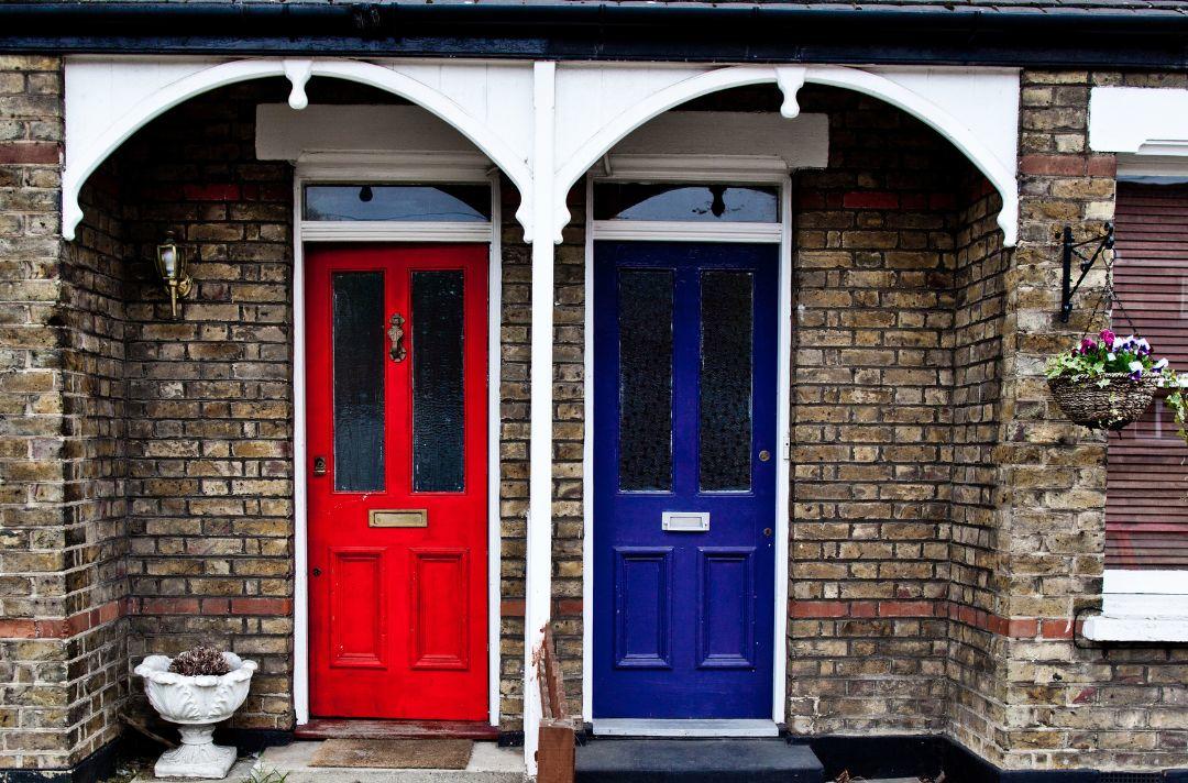 A photo of two neighbouring front doors, one red, one blue.