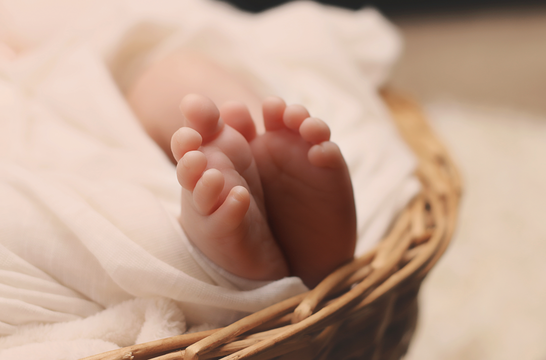 A baby is swaddled in a basket with their feet poking out