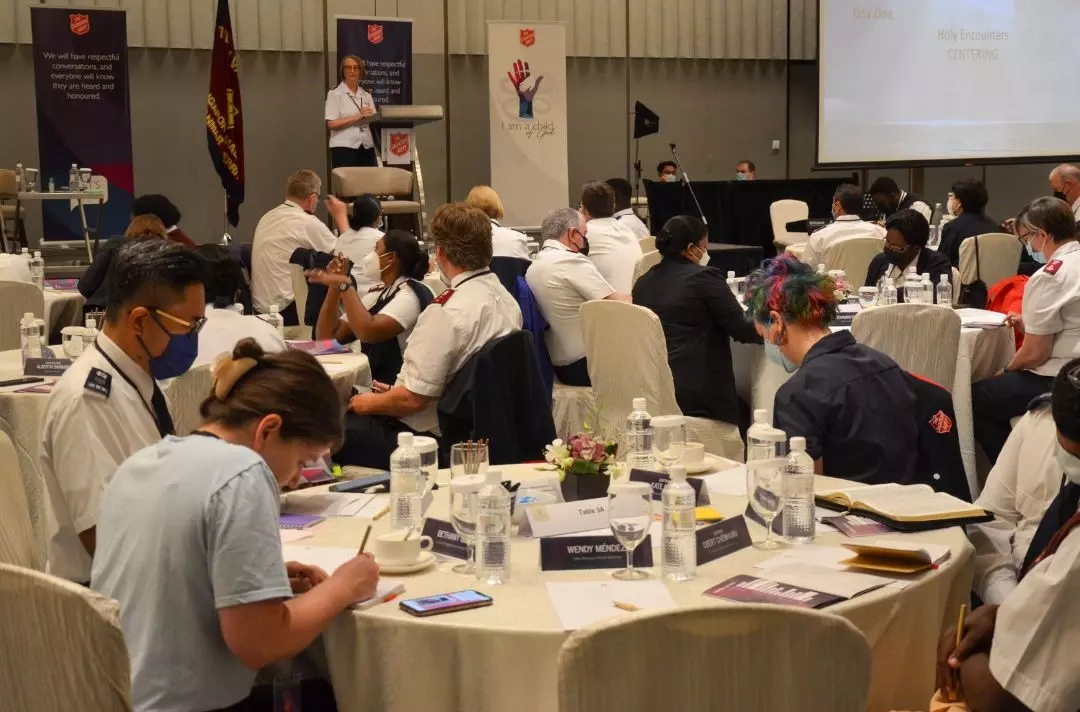 A photo from the International Symposium on Human Sexuality of delegates sitting around tables and making notes while listening to a speaker on a stage