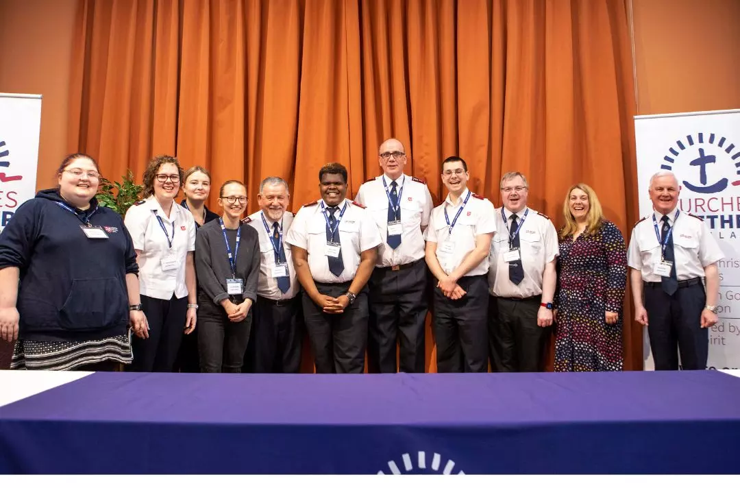 A photo of a group of Salvationists of different ages wearing different styles of uniform in front of Churches Together in England pop-up banners