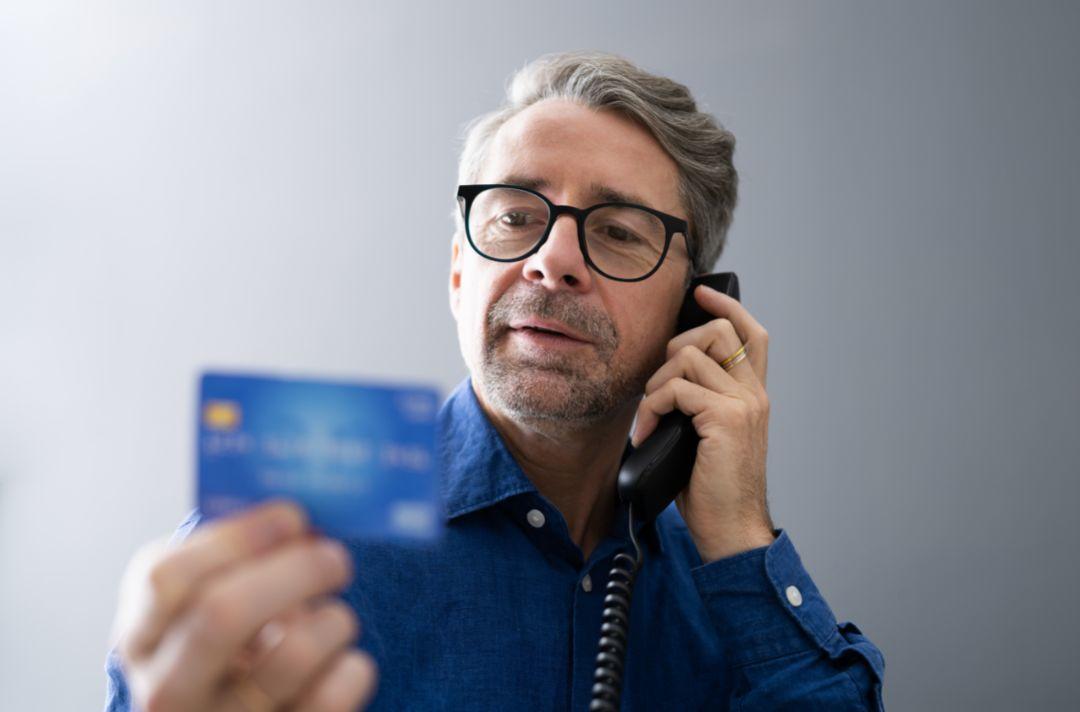 A photo of an older man on the phone holding his credit card