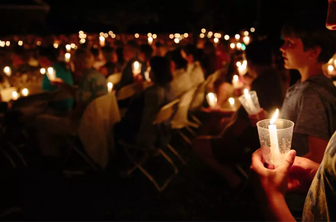 A photo of a church service outside at night with people holding candles