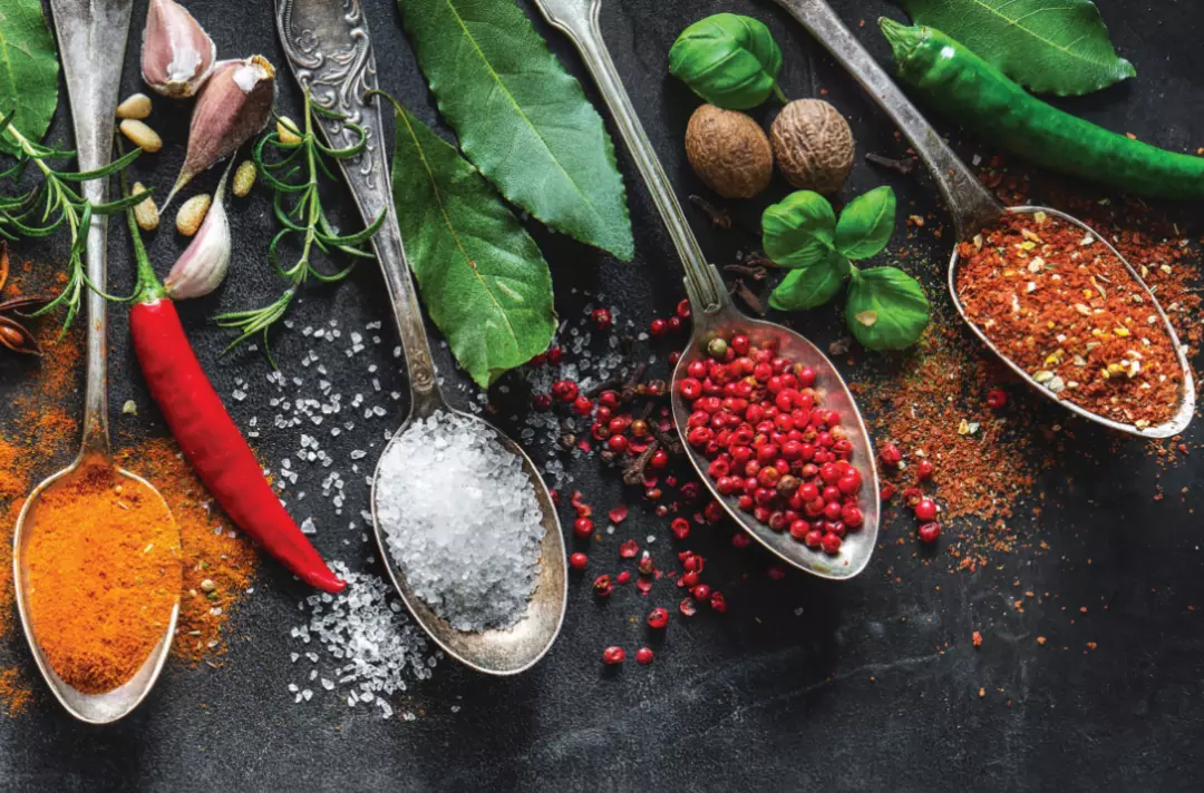 Photo shows spoons displaying a variety of seasonings on a dark background.