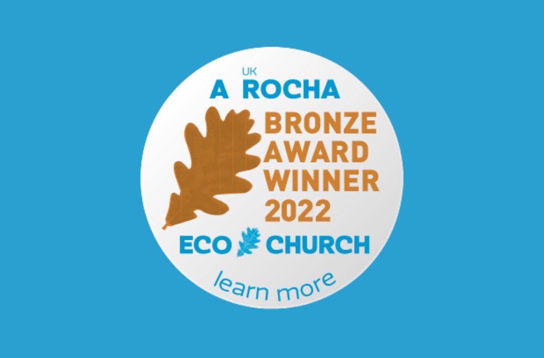 A graphic showing a Eco Church Bronze award sticker featuring a brown leaf. The text reads: 'A Rocha UK Bronze Award Winner 2022. Eco Church. Learn more.'