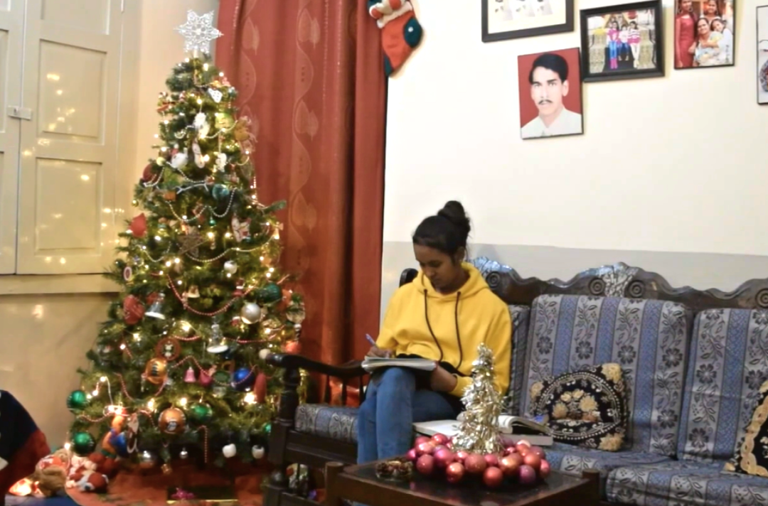Photo shows Joyce sat in a comfortable-looking room with a Christmas tree and decorations. She is studying.