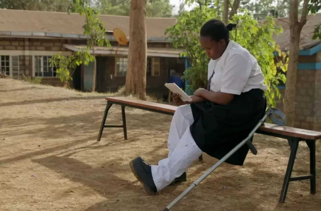Photo shows Josfridah sat on a bench reading.