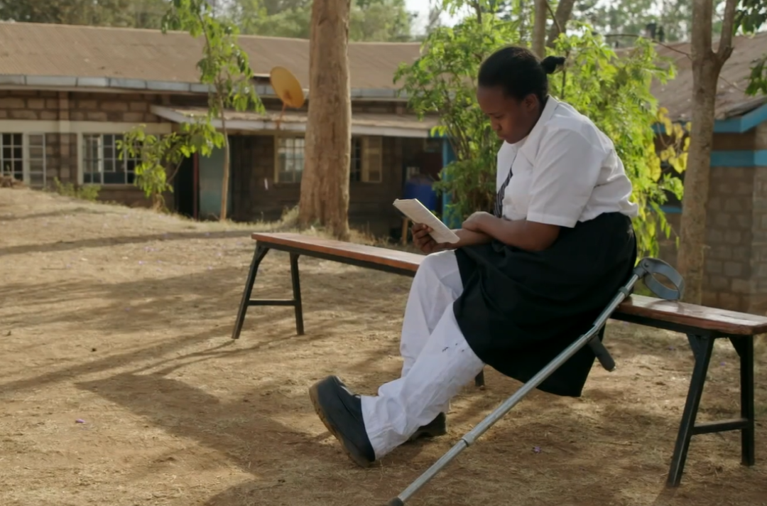 Photo shows Josfridah sat on a bench reading.