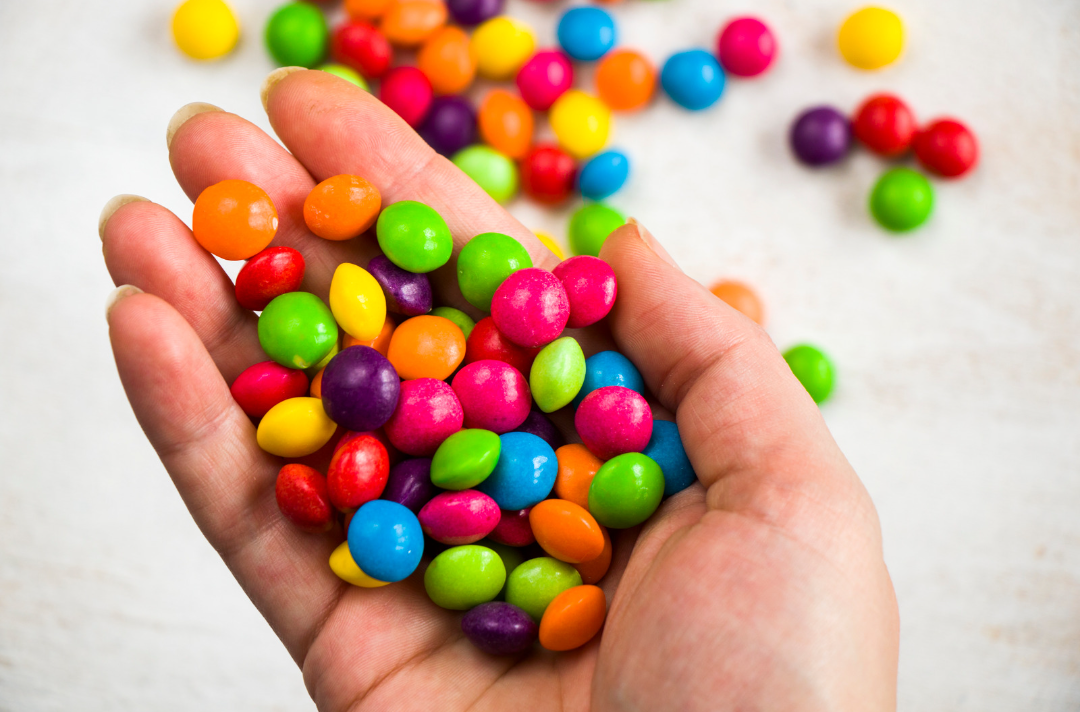 Photo shows an assortment of Skittles sweets cupped in a hand and spilling over a table.