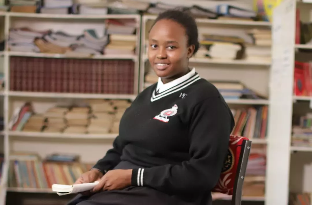 A photo of a black African Salvation Army school girl from holding a book and smiling