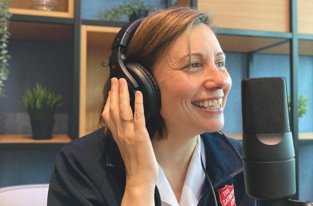 A photo of a Salvation Army officer recording a podcast wearing headphones and speaking into a microphone