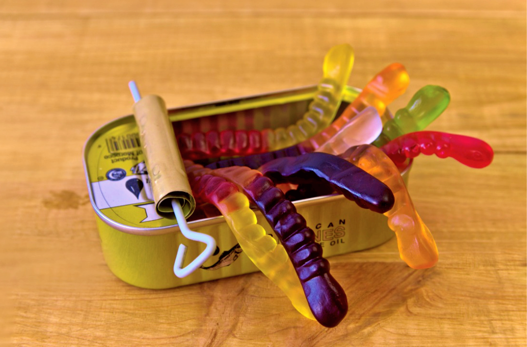 Photo shows a half-open tin with worm-shaped gummy sweets spilling out.