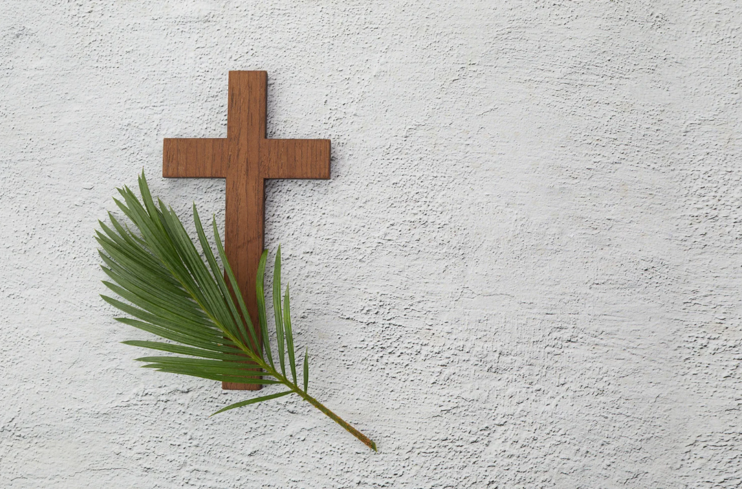 Photo shows a cross and a palm leaf against a light background.